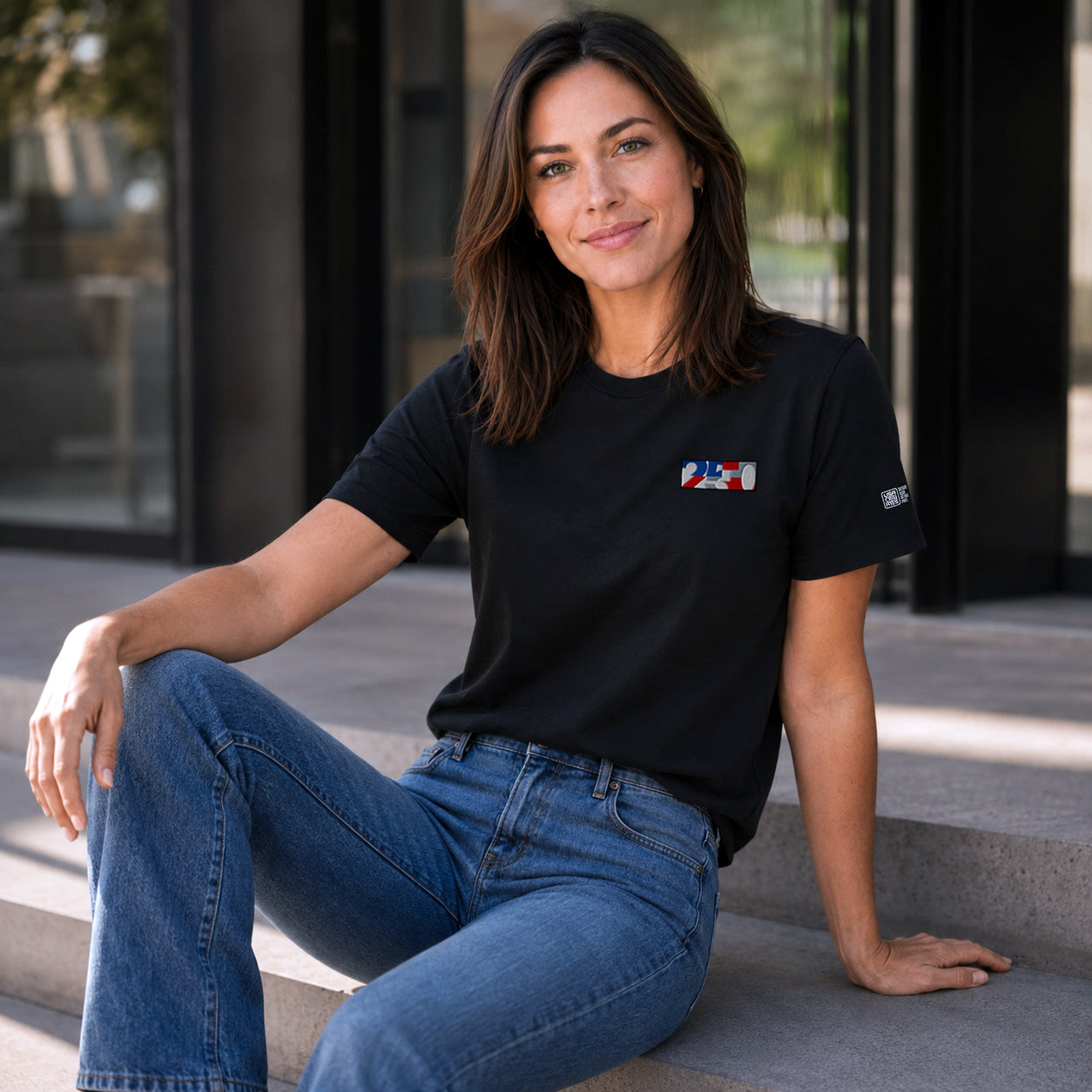 USA CREATES 250 Icon Tee RWB, black tee with RWB 250 chest graphic worn by a woman seated on concrete steps in a relaxed outdoor editorial portrait