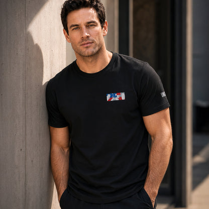 USA CREATES 250 Icon Tee RWB, black tee with RWB 250 chest graphic worn by a man leaning against a concrete wall in an urban editorial portrait