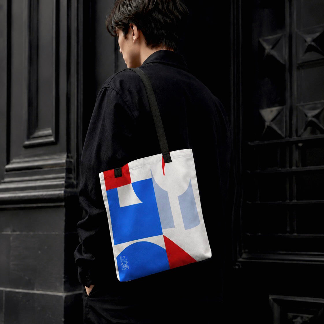 USA CREATES 250 Icon Tote, RWB color-block tote carried over shoulder by a man in black streetwear against a dark architectural doorway